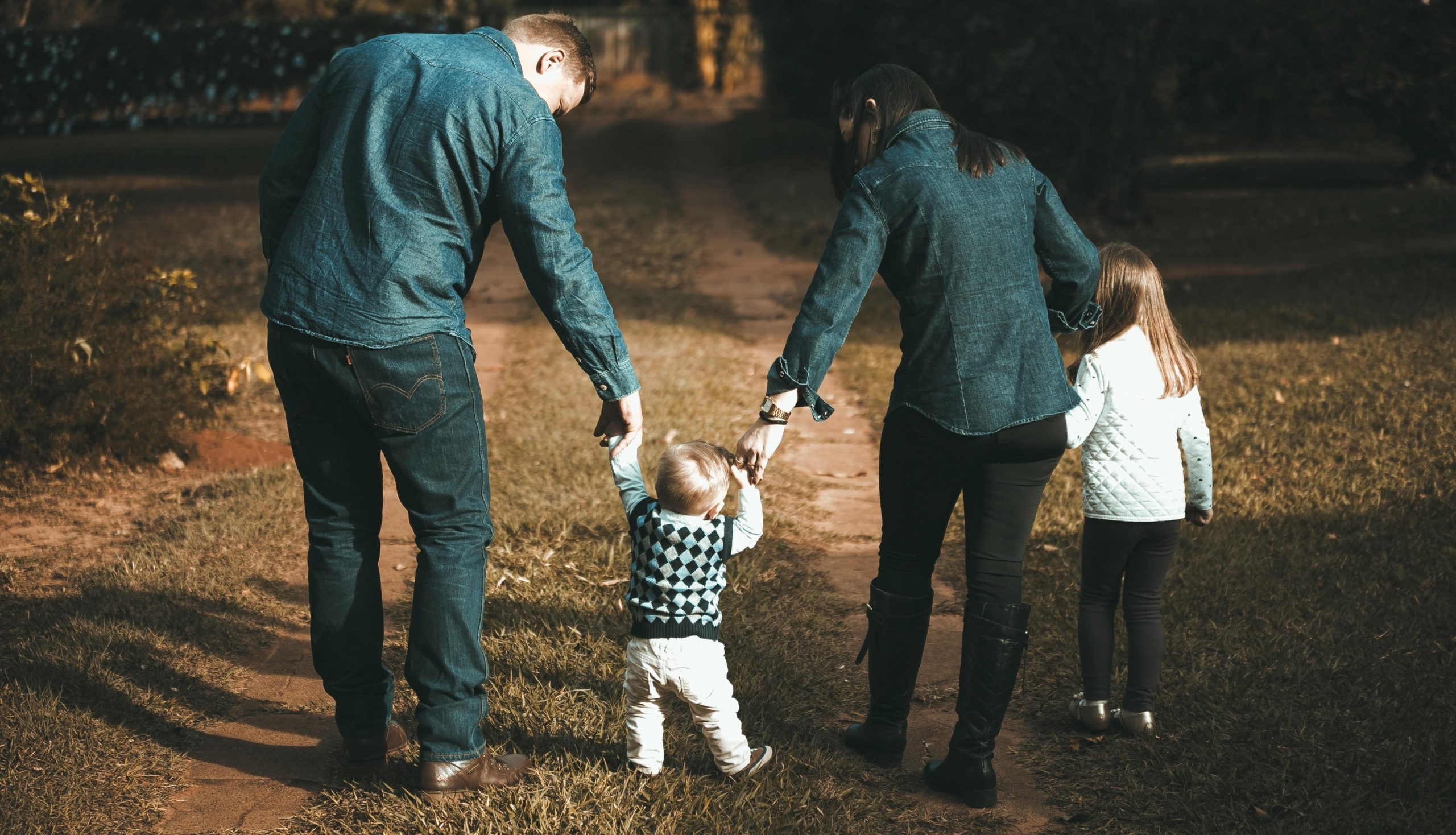 A family of four walks hand in hand on a path, enjoying a sunny day outdoors.