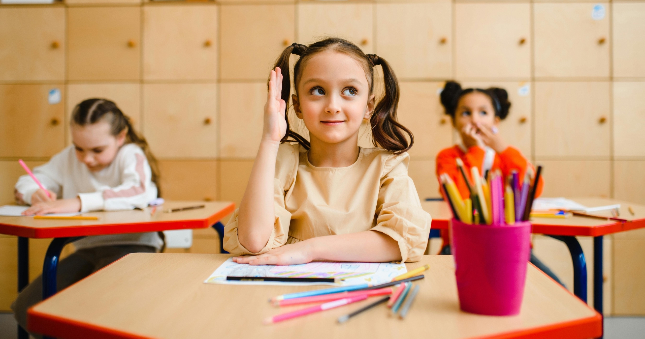 Young girl raises her hand during a lesson in a bright classroom.